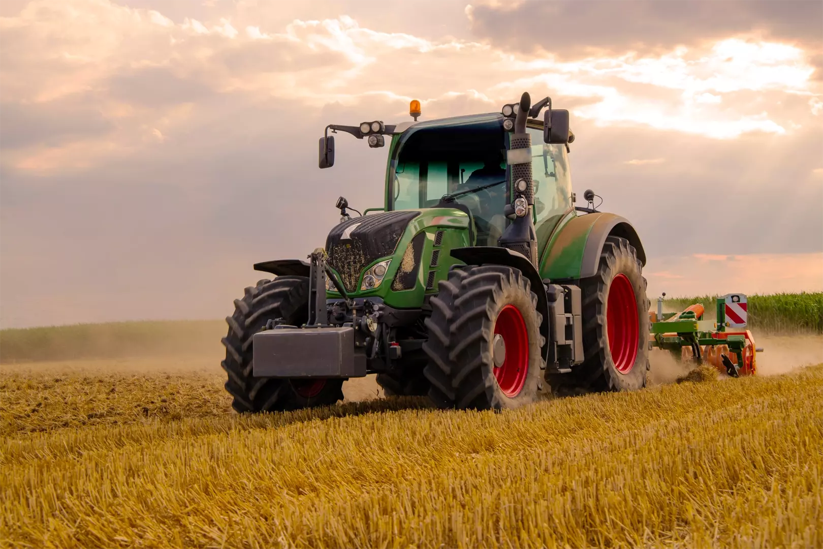 green tractor plowing cereal field with sky with clouds